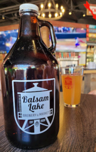 A jug of beer from Balsam Lake Brewery on a table next to a glass.