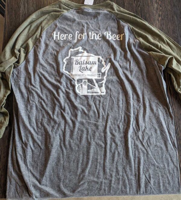 A gray baseball tee with the text "here for the beer" above a graphic of a balsam lake brewery and market label.