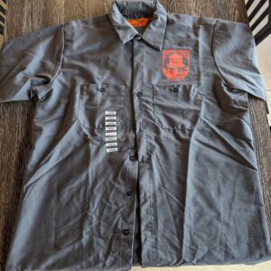 A Brewer's Shirt w/ WI Logo Grey with a badge and name tags on a wooden surface.