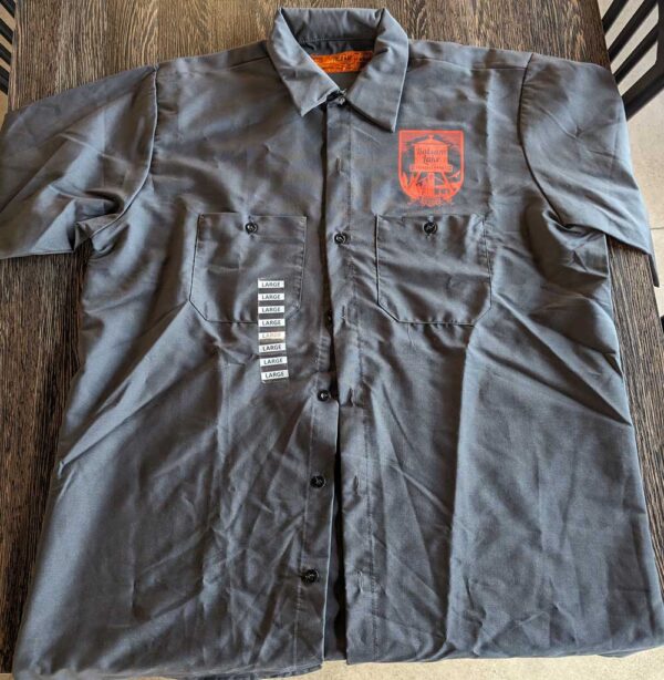 A Brewer's Shirt w/ WI Logo Grey with a badge and name tags on a wooden surface.