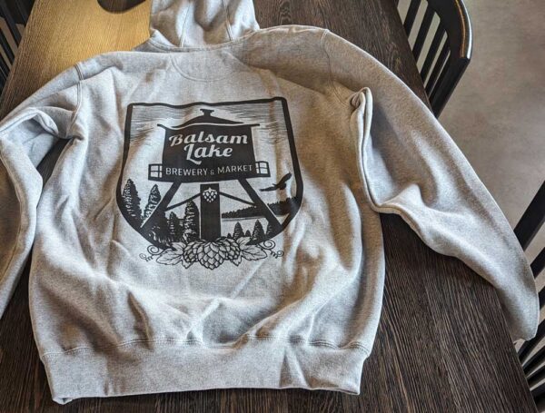 Carhartt Midweight Hoodie with "balsam lake brewery's market" graphic design, lying on a wooden surface.