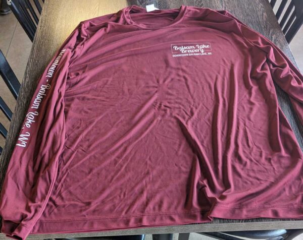 A Maroon Fishing Shirt with text on it laid out on a wooden table.