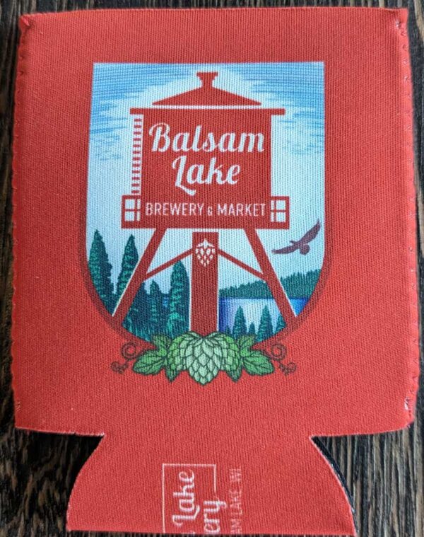 A red Crouler Koozie featuring the balsam lake brewery & market logo with a water tower, trees, hops, and a flying bird design.