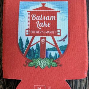 A red Crouler Koozie featuring the balsam lake brewery & market logo with a water tower, trees, hops, and a flying bird design.
