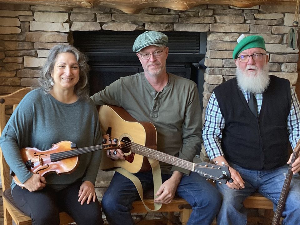 Three people posing with musical instruments in front of a stone fireplace.