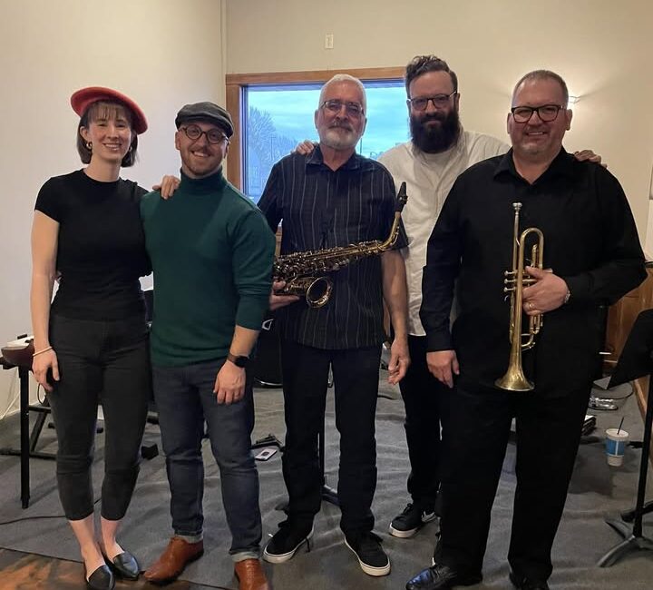 Five people standing indoors, holding a saxophone and a trumpet.